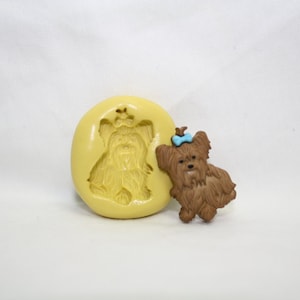 May include: A brown silicone mold of a Yorkshire Terrier with a brown and blue bow. A brown Yorkshire Terrier with a blue bow is shown next to the mold.
