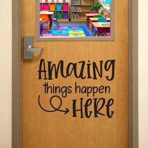 Puede incluir: Una puerta de madera de color marr&oacute;n claro con una ventana rectangular de cristal y un pomo plateado. La puerta presenta letras de vinilo negro que dicen "Amazing things happen HERE" con una flecha decorativa que apunta a "HERE".