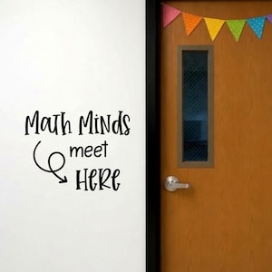 May include: A wall decal with the black text "Math Minds meet HERE" and a curved arrow graphic, positioned next to a wooden door with a rectangular window and a colorful triangular bunting banner hanging across the top of the door frame.
