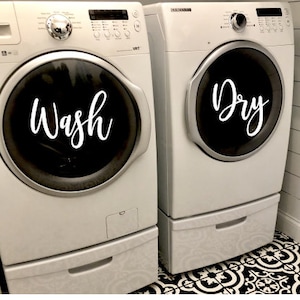 Puede incluir: Dos lavadoras blancas, una con la inscripci&oacute;n "Wash" y la otra "Dry". Las m&aacute;quinas tienen puertas circulares negras y est&aacute;n sobre un suelo con estampado en blanco y negro. Las paredes son blancas.