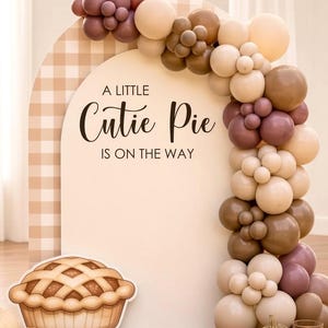 May include: An arched backdrop with a beige gingham pattern and the text A LITTLE Cutie Pie IS ON THE WAY. A balloon garland in shades of cream, tan, and mauve curves over the arch. A cutout of a pie sits at the base with assorted pumpkins.