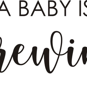 May include: Black and white text on a white background reads "A BABY IS BREWING" in a combination of sans-serif and cursive fonts. The phrase is a pregnancy announcement.
