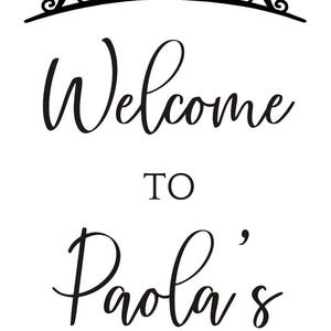 May include: A black and white sign with the words "Welcome to Paola's Quincea&ntilde;era 11.29.2025" in elegant script. A decorative tiara tops the text. The sign is designed for a celebration.