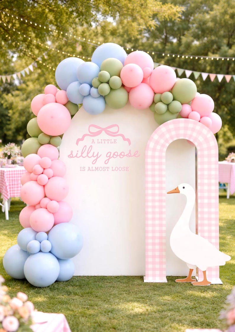 May include: A whimsical party decoration featuring a white arch with a pink and white gingham archway and a large white goose cutout. The arch is adorned with a balloon garland in pastel pink, blue, and green. Text reads "A little silly goose is almost loose."