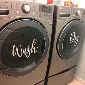 Puede incluir: Dos lavadoras y secadoras plateadas a juego. La puerta de la lavadora tiene la palabra "Wash" en escritura blanca. La puerta de la secadora tiene la palabra "Dry" en escritura blanca. Las m&aacute;quinas est&aacute;n una al lado de la otra.
