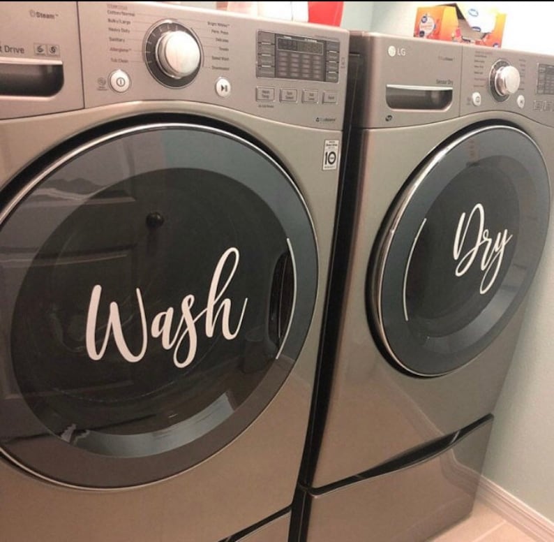 Puede incluir: Dos lavadoras y secadoras plateadas a juego. La puerta de la lavadora tiene la palabra "Wash" en escritura blanca. La puerta de la secadora tiene la palabra "Dry" en escritura blanca. Las m&aacute;quinas est&aacute;n una al lado de la otra.