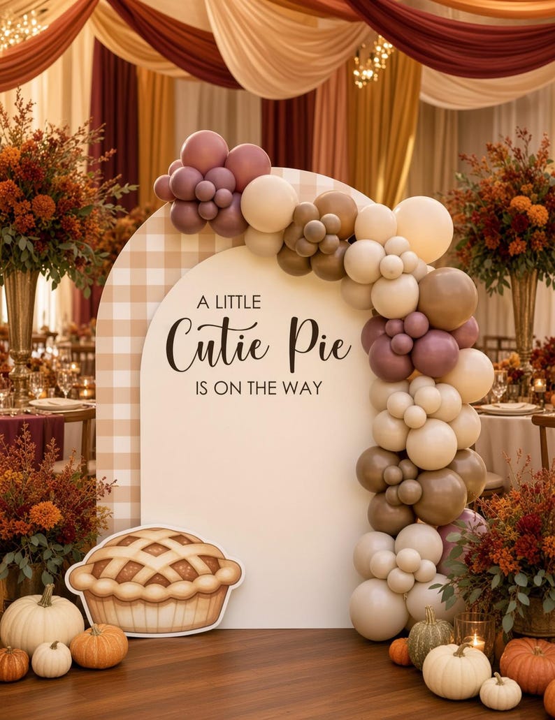 May include: An arched backdrop with a beige gingham pattern and the text A LITTLE Cutie Pie IS ON THE WAY. A balloon garland in shades of cream, tan, and mauve curves over the arch. A cutout of a pie sits at the base with assorted pumpkins.