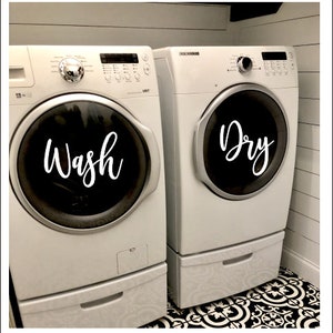 Puede incluir: Dos lavadoras blancas, una con la etiqueta "Wash" y la otra "Dry". Las m&aacute;quinas est&aacute;n una al lado de la otra, con puertas circulares negras. El lavadero tiene un suelo con dibujos en blanco y negro y paredes blancas.