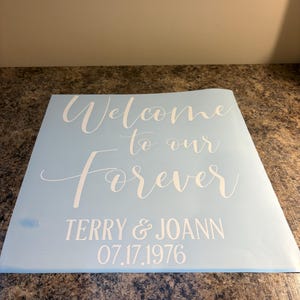 May include: A light blue square decal featuring white text that reads Welcome to our Forever, followed by the names TERRY & JOANN and the date 07.17.1976 in a clean, sans-serif font. The decal has a smooth, matte finish and is ready for application.