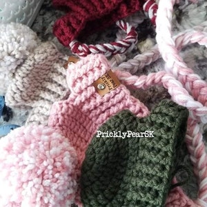 Puede incluir: Una colecci&oacute;n de art&iacute;culos de ganchillo hechos a mano en varios colores. La imagen presenta un art&iacute;culo de ganchillo rojo oscuro con un cord&oacute;n trenzado blanco y rojo, un art&iacute;culo de ganchillo rosa, un art&iacute;culo de ganchillo verde y un pomp&oacute;n rosa y blanco. El texto "PricklyPearSK" es visible.