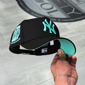 May include: Black baseball cap with a teal New York Yankees logo and a teal underside. The cap features an embroidered patch on the side and the text "Fitted diamonds" on the brim.