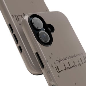 K&ouml;nnte beinhalten: Taupefarbene Handyh&uuml;lle mit schwarzer Kameralinse und dem Zitat: "Licht kann selbst in der dunkelsten H&ouml;lle gefunden werden." Die H&uuml;lle hat ein mattes Finish und ein minimalistisches Design mit Sternakzenten.