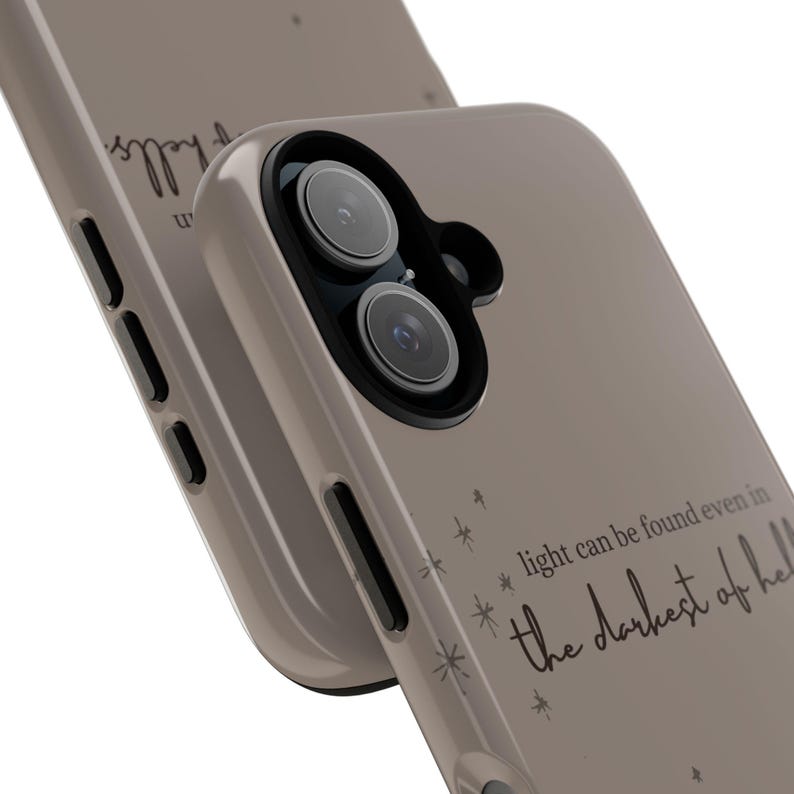K&ouml;nnte beinhalten: Taupefarbene Handyh&uuml;lle mit schwarzer Kameralinse und dem Zitat: "Licht kann selbst in der dunkelsten H&ouml;lle gefunden werden." Die H&uuml;lle hat ein mattes Finish und ein minimalistisches Design mit Sternakzenten.