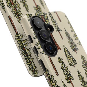 May include: A phone case with a repeating pattern of stylized evergreen trees in shades of green and brown on a cream background. The case has a black camera module with three lenses and a flash. The design is repeated on the second case.