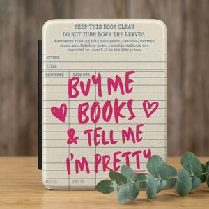 May include: A rectangular e-reader case with a cream-colored background featuring a vintage library checkout card design. The text reads: KEEP THIS BOOK CLEAN, DO NOT TURN DOWN THE LEAVES, and BUY ME BOOKS & TELL ME I'M PRETTY in bright pink.