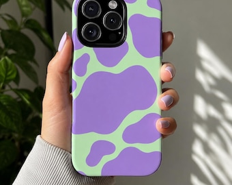 May include: A smartphone case with a light green background and large, irregular purple shapes. The case has a glossy finish and a camera cutout. The phone case is held in a hand.