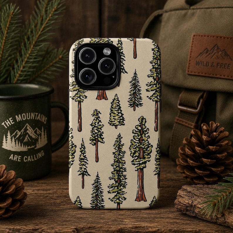 May include: A phone case with a repeating pattern of green and brown trees on a beige background. The phone case is next to a green mug with the text "THE MOUNTAINS ARE CALLING" and a backpack with a "WILD & FREE" patch.