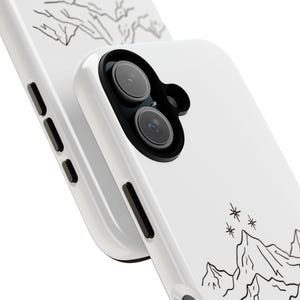 K&ouml;nnte beinhalten: Wei&szlig;es Handycase mit einem schwarzen Bergketten- und Sterndesign. Das Case hat eine gl&auml;nzende Oberfl&auml;che und verf&uuml;gt &uuml;ber einen Ausschnitt f&uuml;r eine Dual-Objektiv-Kamera. Das Design ist eine minimalistische Illustration einer Berglandschaft.