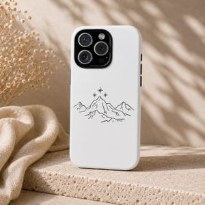 K&ouml;nnte beinhalten: Wei&szlig;es Handycase mit einer schwarzen Strichzeichnung von Bergen und Sternen. Das Case hat eine gl&auml;nzende Oberfl&auml;che und einen Kameraausschnitt mit mehreren Linsen. Das Design ist schlicht und elegant, passend f&uuml;r Outdoor-Enthusiasten.