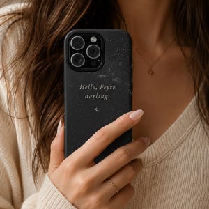 K&ouml;nnte beinhalten: Schwarze Handyh&uuml;lle mit Sternennacht-Design und dem Text "Hello, Feyre darling." Die H&uuml;lle hat eine matte Oberfl&auml;che und eine kleine Halbmond-Grafik. Die Handyh&uuml;lle wird von einer Person gehalten.