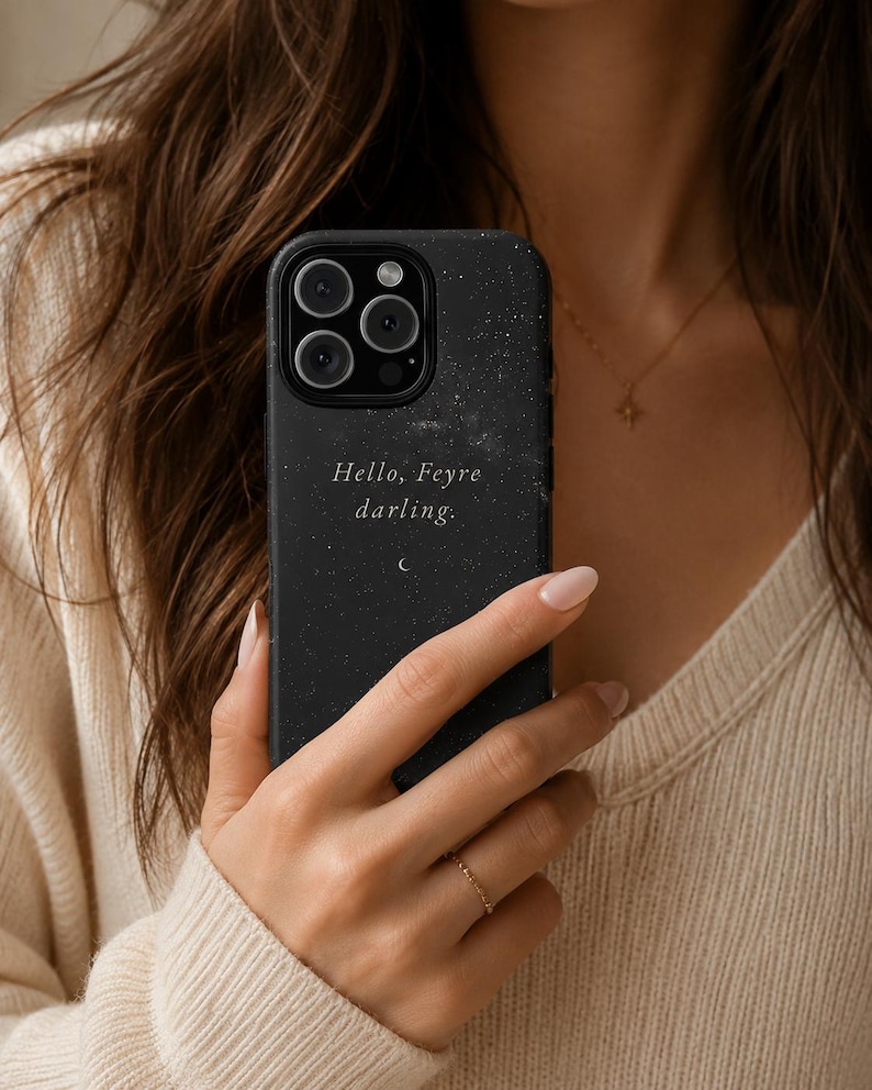 K&ouml;nnte beinhalten: Schwarze Handyh&uuml;lle mit Sternennacht-Design und dem Text "Hello, Feyre darling." Die H&uuml;lle hat eine matte Oberfl&auml;che und eine kleine Halbmond-Grafik. Die Handyh&uuml;lle wird von einer Person gehalten.