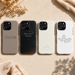 K&ouml;nnte beinhalten: Vier Telefonh&uuml;llen in einer Reihe, jede mit einem anderen Design. Die erste ist taupefarben mit Text, die zweite ist schwarz mit Text, die dritte ist cremefarben mit einem Bergmotiv und die vierte ist wei&szlig; mit einem Bergmotiv.