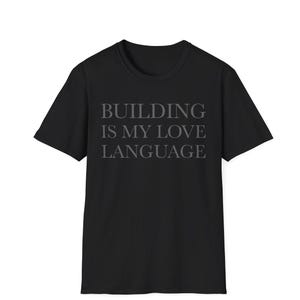 Può includere: Una t-shirt nera a maniche corte con il testo "BUILDING IS MY LOVE LANGUAGE" stampato in un carattere serif grigio scuro al centro del petto. Il capo presenta un classico girocollo e una vestibilità standard con maniche corte.