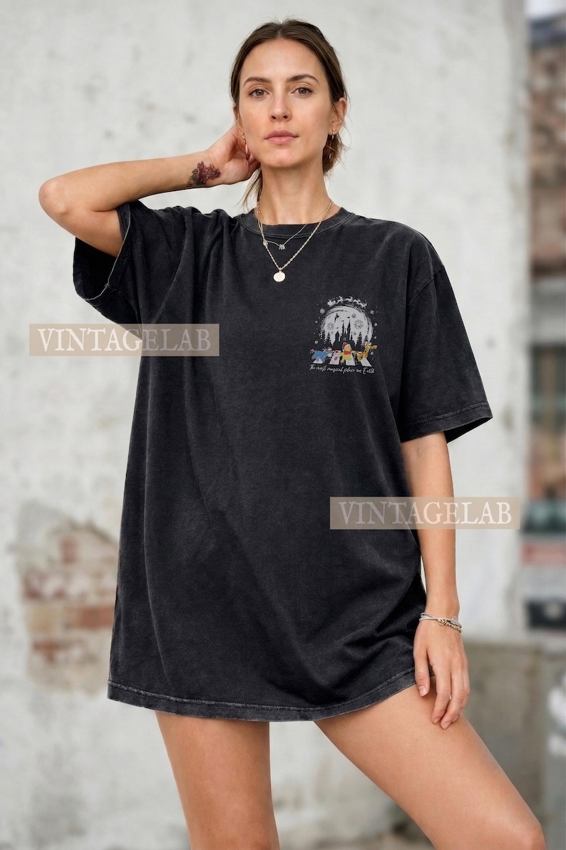 Op de afbeelding: Zwart T-shirt met een grafische print van een nachtelijke bossc&egrave;ne met cartoonfiguren en de tekst "The most magical place on earth". Het shirt heeft korte mouwen en een relaxte pasvorm.