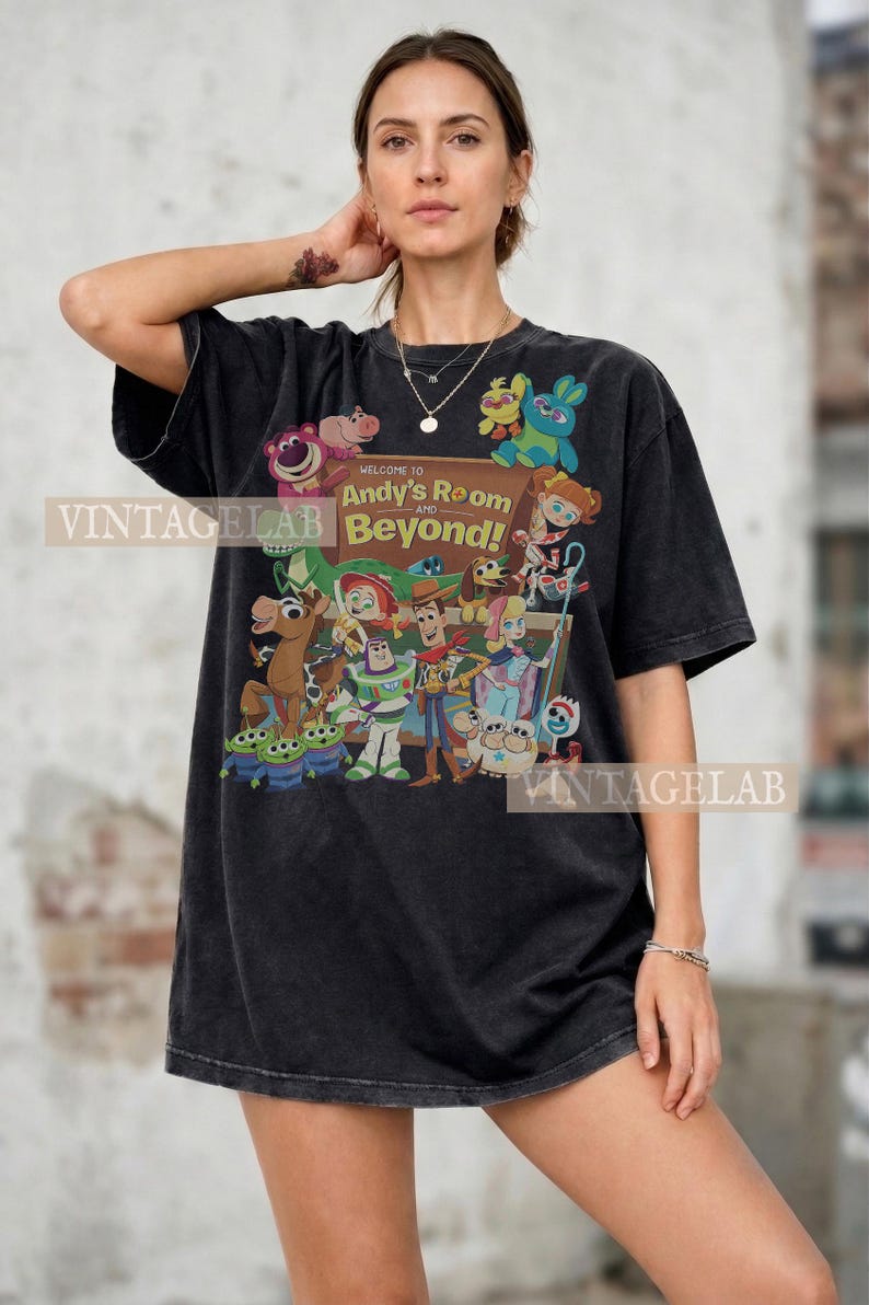 K&ouml;nnte beinhalten: Schwarzes T-Shirt mit einer farbenfrohen Grafik von Charakteren aus dem Film "Toy Story". Das Design enth&auml;lt den Text "Welcome to Andy's Room and Beyond!". Das Shirt hat eine lockere Passform und kurze &Auml;rmel.