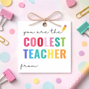 Peut inclure: Une carte carrée blanche avec le texte "you are the COOLEST TEACHER" en lettres colorées. La carte est attachée avec de la ficelle et entourée d'articles de papeterie roses et jaunes, dont des trombones et des pinces à reliure. Une illustration de crayon est dans le coin supérieur droit.