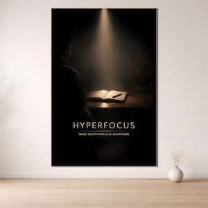 Peut inclure: Une affiche sombre avec le mot "HYPERFOCUS" en lettres dorées. En dessous, le texte indique "WHEN EVERYTHING ELSE DISAPPEARS". Un livre ouvert et un stylo reposent sur une surface en bois, éclairés par un projecteur. Une silhouette est visible.