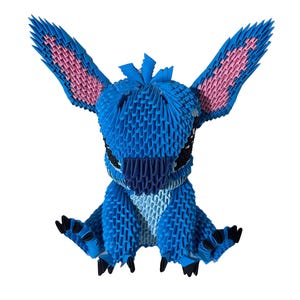 May include: A blue origami figure of a cartoon character with large ears and black eyes. The ears have pink inner details. The figure is sitting with its arms outstretched, and its feet are black.