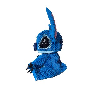 May include: A blue origami figure of a cartoon character with large ears and black eyes. The figure is sitting down with its arms and legs in front. The origami is made of many small, folded pieces of paper.