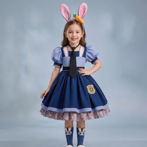 May include: A young girl in a blue dress with a black tie, a badge, and bunny ear headband. The dress has a layered skirt and short, puffy sleeves. The socks have bunny faces. The outfit is a costume.