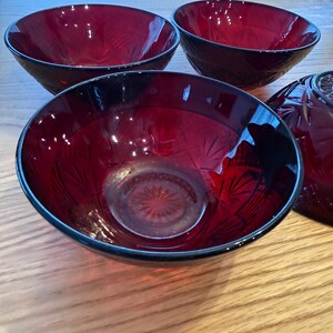 Peut inclure: Un ensemble de quatre bols en verre rouge profond présentant un motif d'étoile pressé sur la base et des motifs en éventail rayonnants sur les parois extérieures. Les bols ont un bord circulaire lisse et une finition rubis translucide.