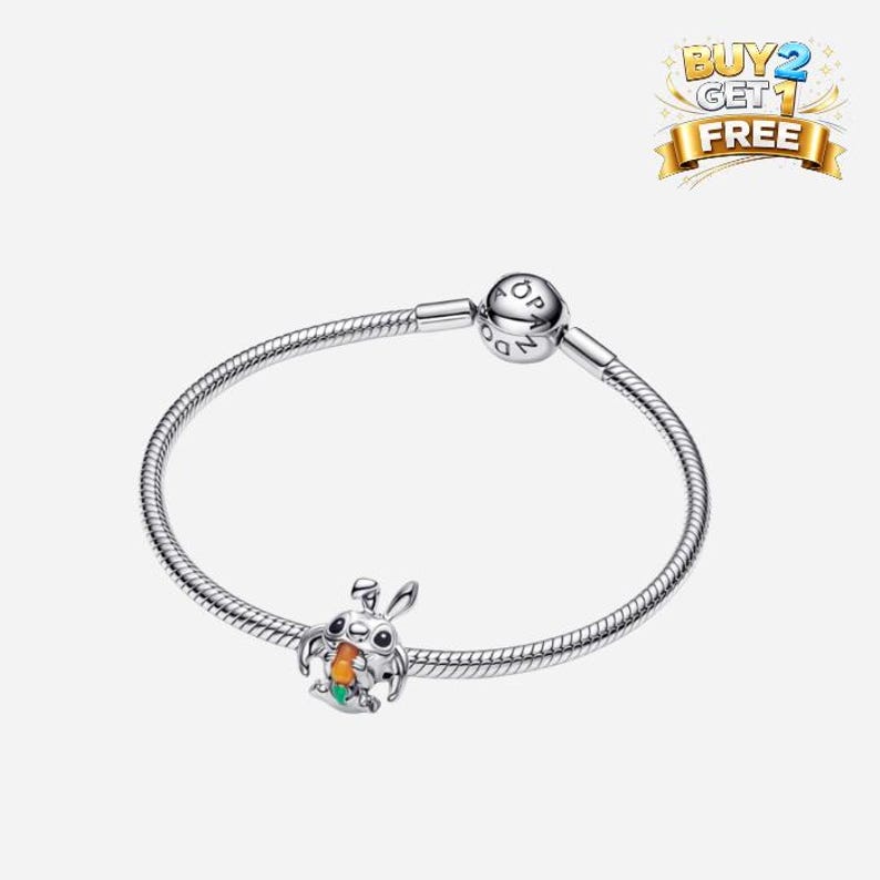 Pode incluir: Uma pulseira de prata com um berloque de coelho de desenho animado segurando uma cenoura. O berloque tem detalhes em laranja, verde e branco. A pulseira tem um fecho redondo com as letras "OP". Uma faixa "Compre 2 Leve 1 Gr&aacute;tis" est&aacute; no canto superior direito.