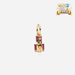 May include: A gold-colored charm in the shape of a nutcracker soldier. The charm has a pink hat and accents, with a star-shaped gem. The soldier's uniform is detailed with black and white elements. The charm is suspended from a gold loop.
