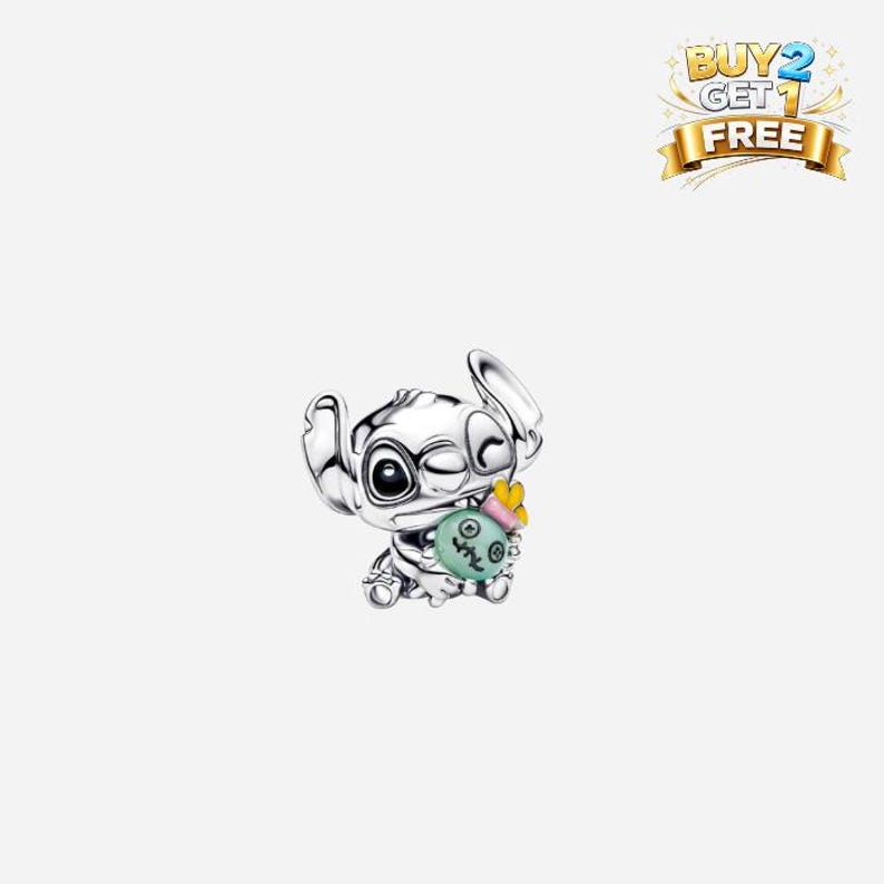 May include: A silver-colored charm featuring the character Stitch from Lilo & Stitch. Stitch is winking and holding a green and blue object with a yellow bow. The charm has a "BUY 2 GET 1 FREE" banner.