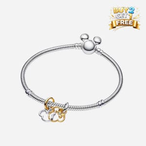 May include: A silver bracelet with a Mickey Mouse head clasp and two charms. One charm is a gold and silver Mickey Mouse head, and the other is a gold Mickey Mouse head with a small clear gem. The bracelet has a Buy 2 Get 1 Free banner in the top right corner.