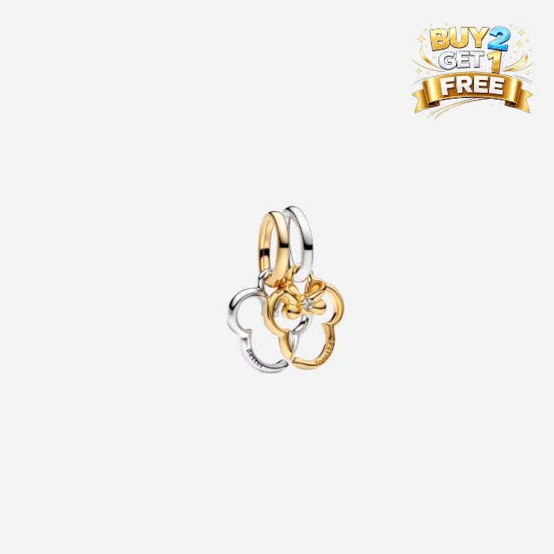 May include: A gold and silver charm featuring two Mickey Mouse head silhouettes. One charm is gold-toned, the other is silver-toned. The charms are connected by a gold and silver ring. A small diamond-like stone is set in the gold charm.