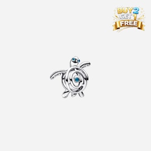 Puede incluir: Un charm de tortuga plateada con detalles azules. El charm presenta un diseño estilizado con un caparazón en espiral y pequeñas aletas. Los ojos de la tortuga también son azules. El charm está sobre un fondo blanco.