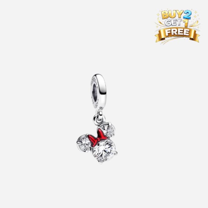 K&ouml;nnte beinhalten: Ein silberner Charm mit einem Minnie Mouse-Design. Der Charm hat eine rote Schleife und drei klare, funkelnde Zirkonia-Steine. Der Charm ist an einer silbernen Schlaufe aufgeh&auml;ngt. Das Bild enth&auml;lt auch ein Banner "KAUFE 2 BEKOMME 1 GRATIS".