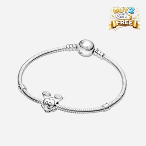 Puede incluir: Una pulsera plateada con un charm de Mickey Mouse. La pulsera tiene un dise&ntilde;o de cadena de serpiente con un cierre redondo y un charm de Mickey Mouse. El charm es una representaci&oacute;n detallada de la cara de Mickey. La imagen tambi&eacute;n incluye una pancarta de "COMPRA 2 Y LL&Eacute;VATE 1 GRATIS".