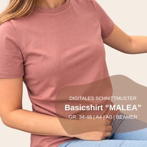 Puede incluir: Una camiseta de manga corta color rosa empolvado con cuello redondo. Un gráfico superpuesto marrón contiene el texto: DIGITALES SCHNITTMUSTER Basicshirt MALEA GR. 34-48 A4 A0 BEAMER. La camiseta se lleva con unos vaqueros azul claro.