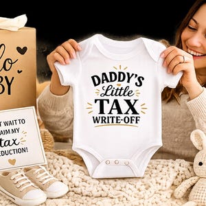 May include: A white baby onesie with the text "DADDY'S Little TAX WRITE-OFF" in black and gold. The image also includes a "hello BABY" gift box, a sign that says "CAN'T WAIT TO CLAIM MY tax DEDUCTION!", and baby shoes.