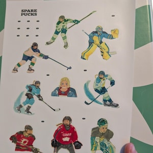 May include: A sheet of stickers featuring hockey players in action. The stickers depict players in various uniforms, including green, blue, and red, with hockey sticks and pucks. The text "SPARE PUCKS" is at the top.