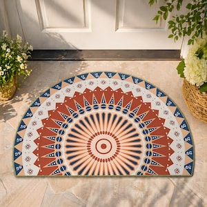 May include: A half-circle doormat with a geometric design. The mat features a central circular pattern in shades of orange and red, surrounded by blue, white, and tan geometric shapes. The border is a dark green.