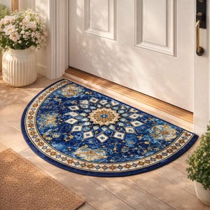 Puede incluir: Una alfombra de media luna con un detallado estampado floral azul y dorado. La alfombra presenta un diseño de medallón central y un borde decorativo. La alfombra está colocada frente a una puerta blanca, añadiendo un toque de elegancia a la entrada.