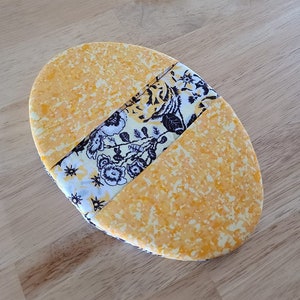 May include: A yellow oval-shaped fabric coaster with a black and white floral pattern.