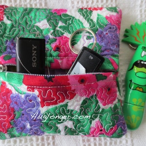 May include: A small floral fabric pouch with a zipper closure. The pouch is filled with a black USB drive labeled "SONY" and a black key fob. A green cartoon character keychain is visible to the right of the pouch.